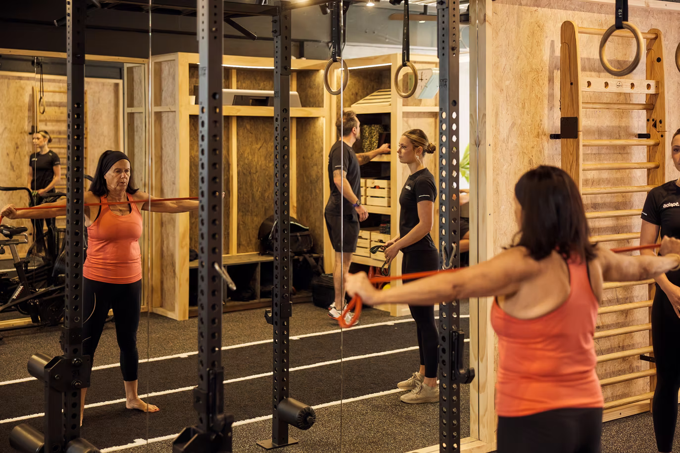 Client holding a red resistance band at shoulder height, seen in the gym mirror, at Adapt, North Sydney