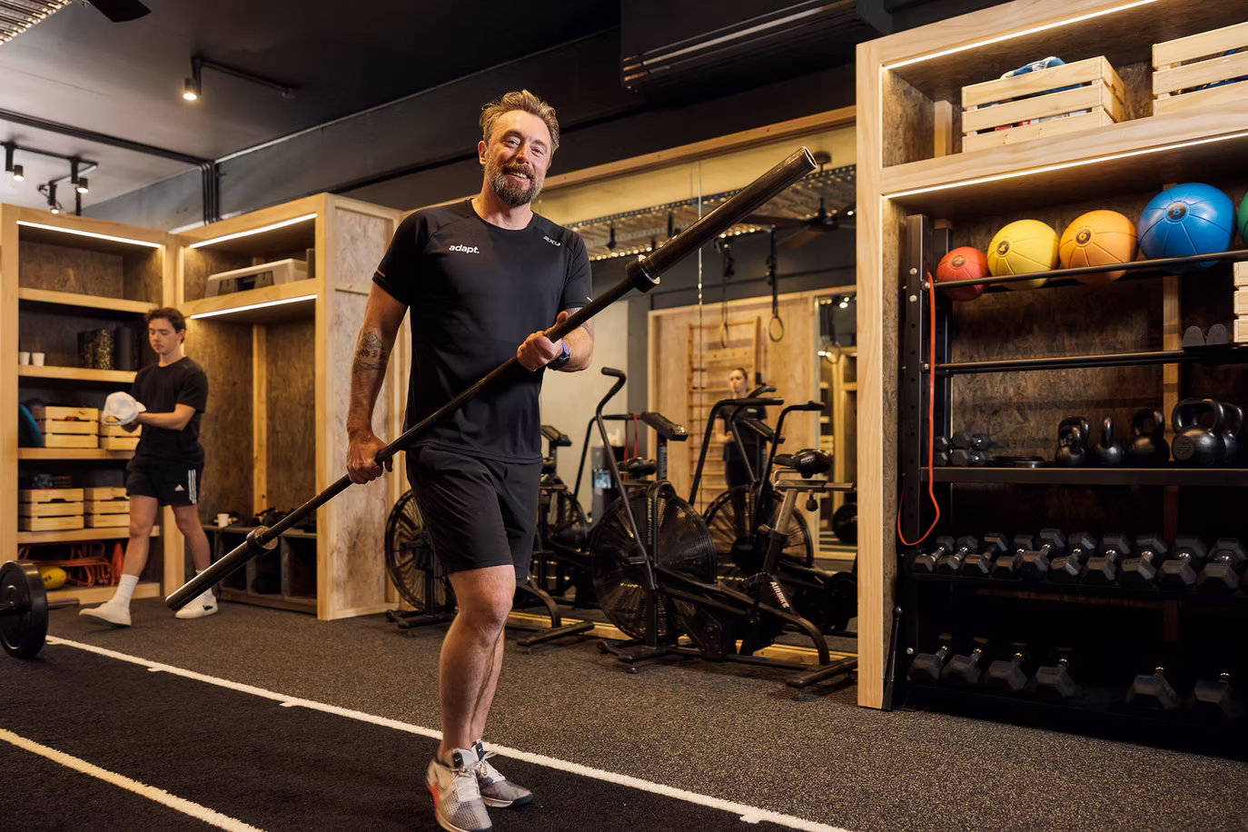 Coach carrying a loaded barbell between racks before a coached session at Adapt, North Sydney