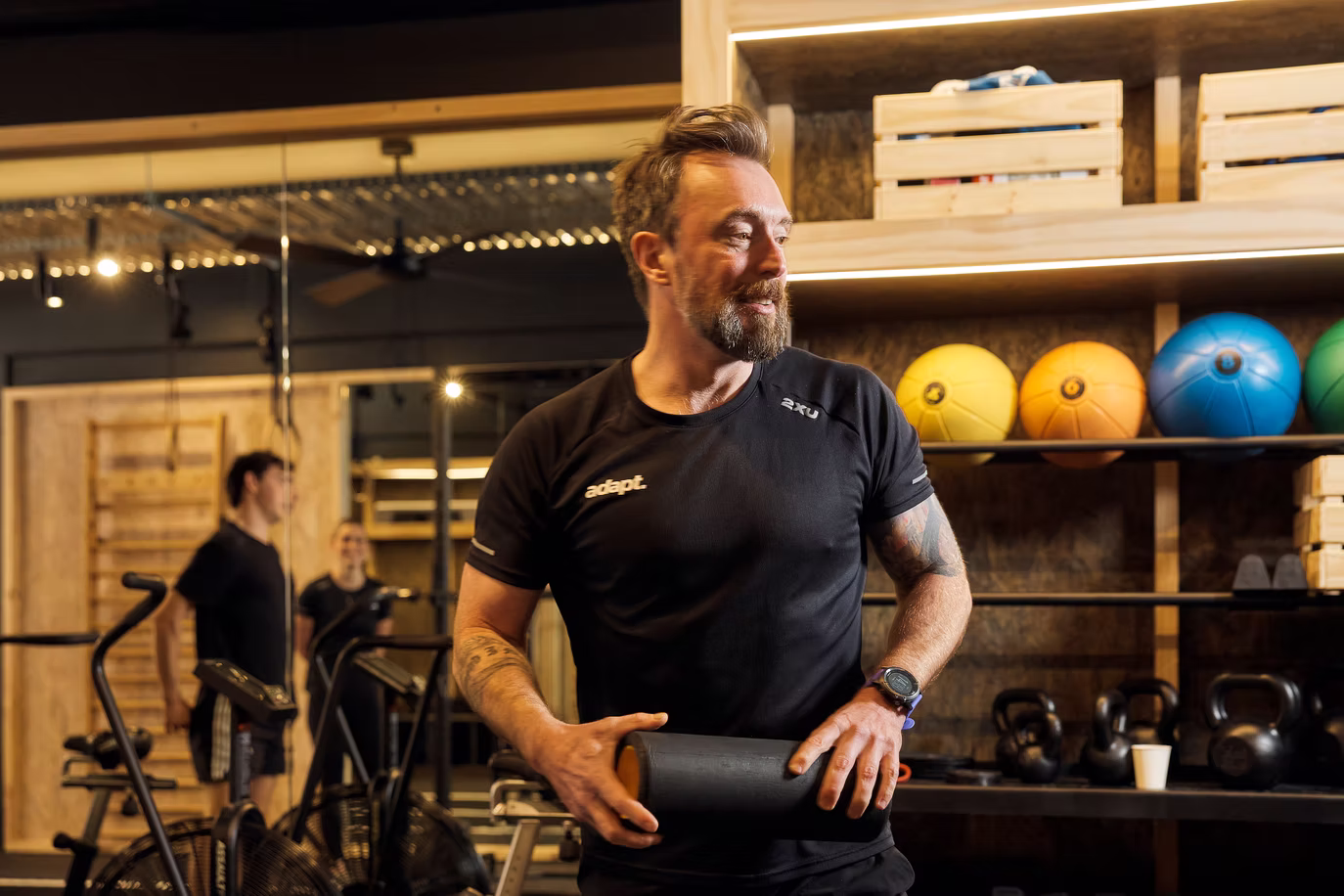 James Bowen holding a black foam roller in front of medicine balls and kettlebells at Adapt, North Sydney
