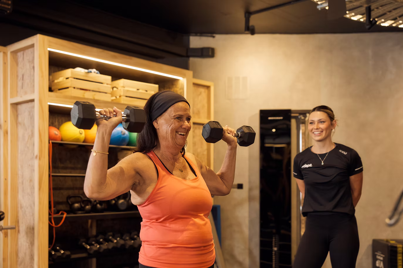 Client doing a shoulder press while a trainer watches at Adapt, North Sydney